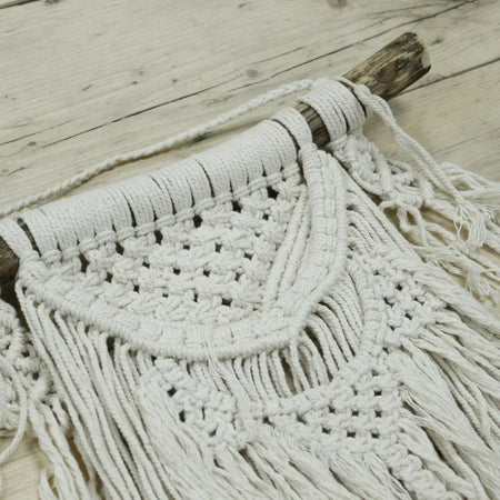 A white macrame wall hanging with intricate woven patterns and long fringe made from natural fiber rope