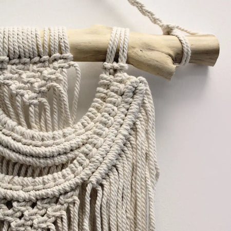 Cream-colored macrame wall hanging two waves with intricate knotting on natural wood dowel for home decor