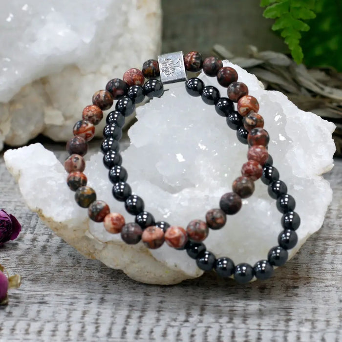 A pair of magnetic gemstone bracelets with red and black beads and silver clasp displayed on a white crystal
