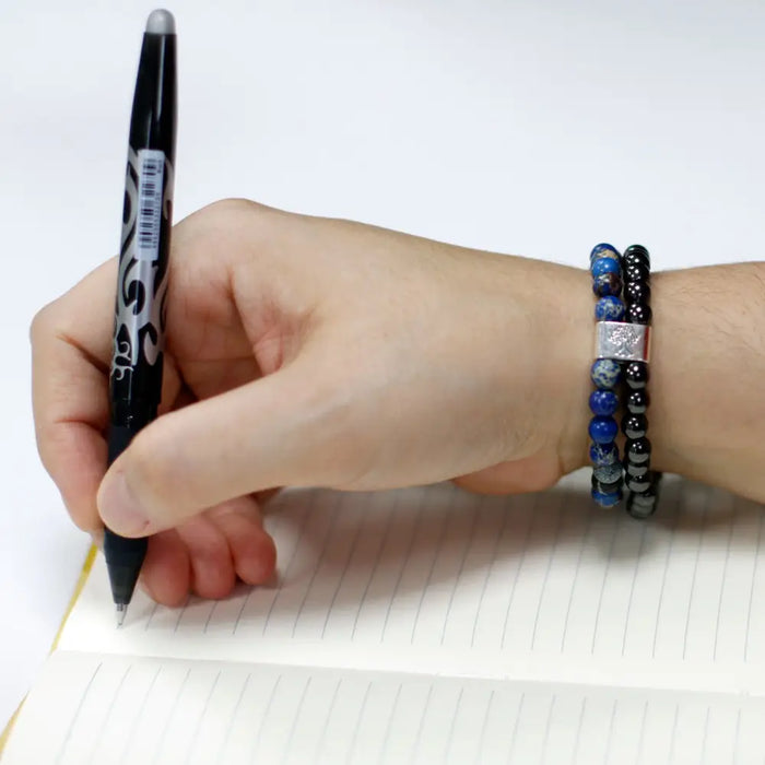 Black and silver marker with patterned grip held over lined paper next to a magnetic gemstone bracelet sodalite