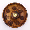 A round mango wood incense burner disc with a brass center and seven engraved chakra symbols around the edge