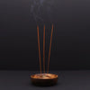Wooden mango wood incense stick burner disc with yin and yang symbol holding three brown wood incense sticks with smoke