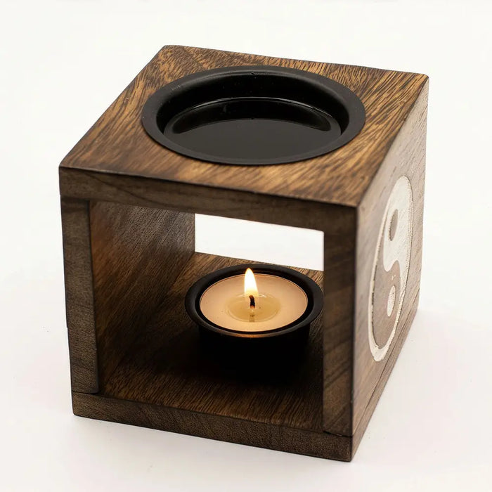 Dark mango wood oil burner cube with yin yang symbol and black top holding a lit tealight candle inside