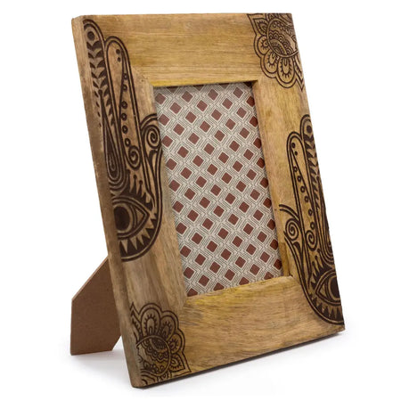 A rustic mango wood picture frame with dark brown hand carved hamsa symbols and floral patterns on a matching easel base