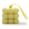 Pale yellow cube-shaped massage soap with rounded bumps and a matching yellow strap for hanging peach and lemon scent