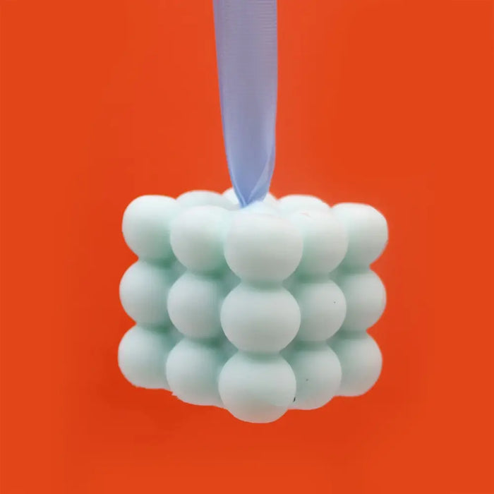 A mint green silicone massage soap cube with a soft texture and light blue ribbon looped through the top