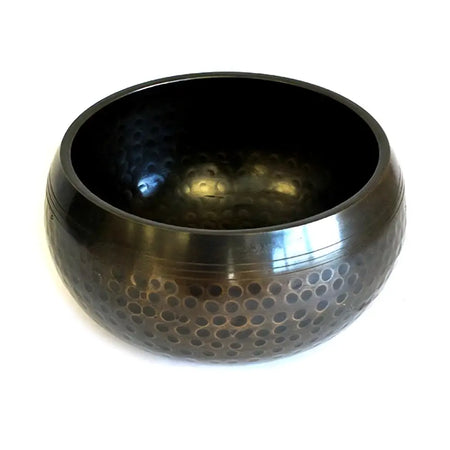 A medium black beaten brass singing bowl with a dark hammered exterior and smooth inner surface with indentations