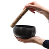 Medium black beaten brass singing bowl made of hammered metal with wooden mallet sitting on a plain surface