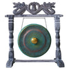 A verdigris-finished bronze gong with golden center hanging on a carved dark gray wooden stand with dragon motifs