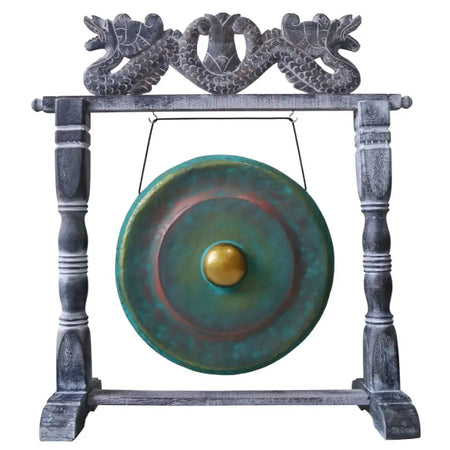 A verdigris-finished bronze gong with golden center hanging on a carved dark gray wooden stand with dragon motifs