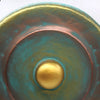 A hand-forged copper medium gong with turquoise patina and polished gold center on a green wash stand 50cm