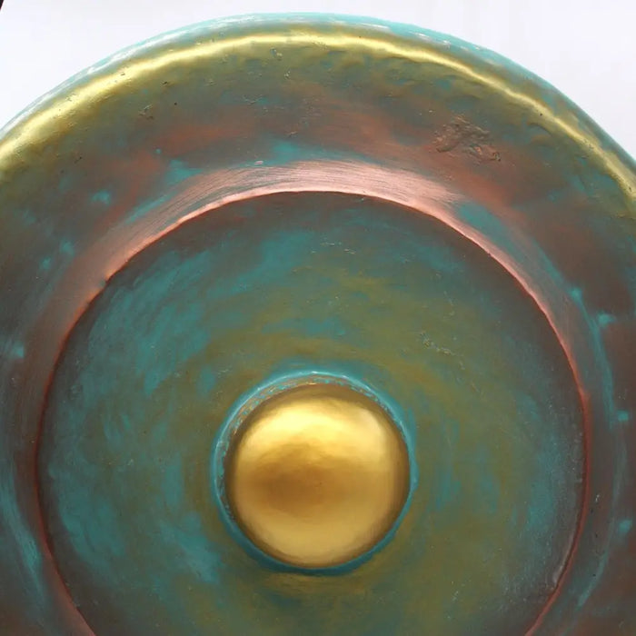 A hand-forged copper medium gong with turquoise patina and polished gold center on a green wash stand 50cm