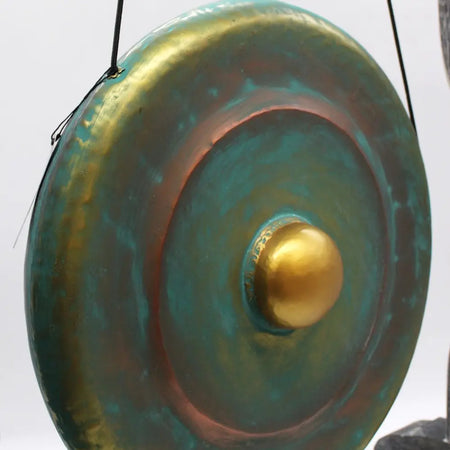 A 50cm bronze gong with a green patina and golden boss on a wooden stand showing circular ridges