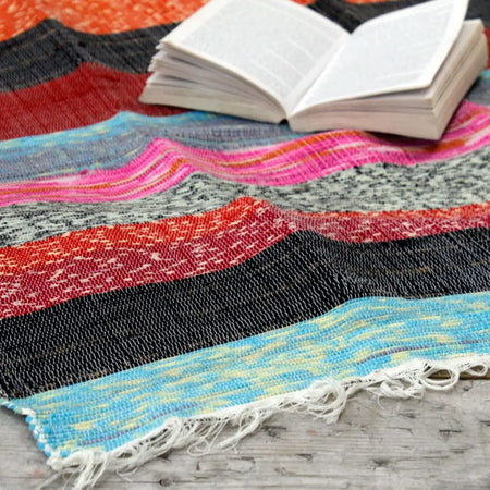 Medium luxury rag rug with bold red black turquoise pink and gray stripes and frayed white edge in natural bands style