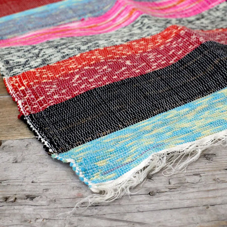 Medium luxury rag rug with natural bands featuring textured pink red black and blue stripes and white fringe