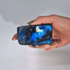 A hand holds a polished blue madagascar labradorite stone 8-10cm with swirling patterns and an iridescent sheen