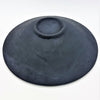 A matte black handcrafted ceramic bowl with a smooth textured surface and a central indentation in a medium mosaic tile dish green setting