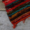 Medium orange rag rug with vibrant multicolored woven pattern frayed edges and rustic handcrafted texture