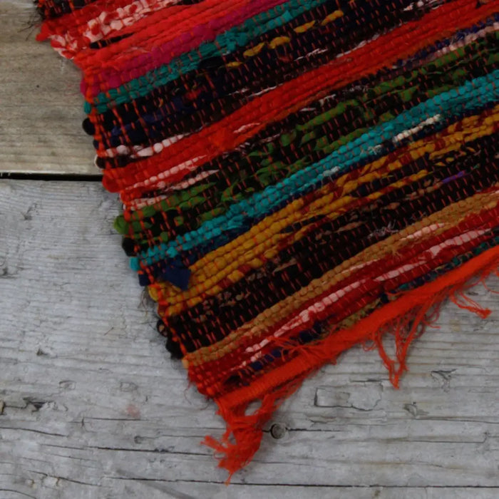 Medium orange rag rug with vibrant multicolored woven pattern frayed edges and rustic handcrafted texture