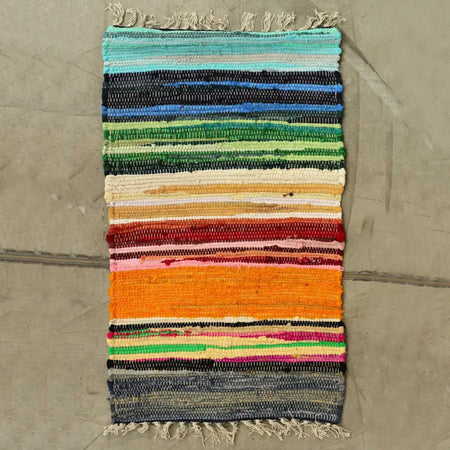 Medium rag rug handwoven with rainbow colours in vibrant stripes and fringed edges made from cotton fibers