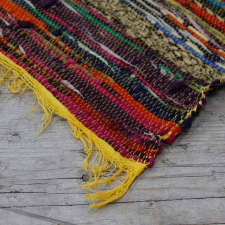 Medium rag rug with multicolored stripes and frayed yellow edges made of handwoven fabric in rag rugs style