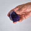 A hand holding a medium rich colour amethyst crystal point with deep purple faceted surface and speckled interior