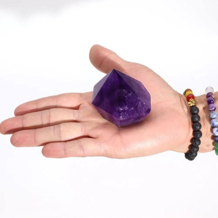 A deep purple amethyst crystal point with a faceted geometric shape resting in an open palm weighing 139g approx