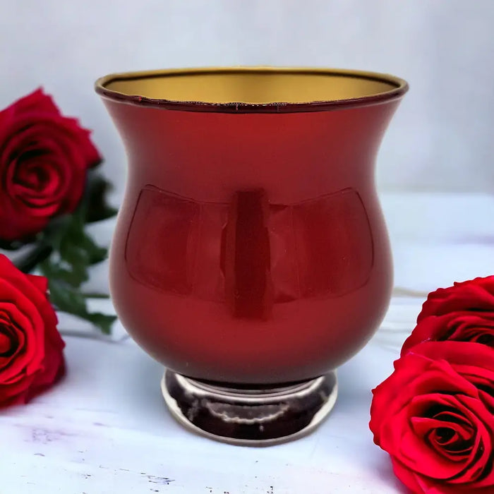 A glossy metallic red glass tealight holder with a gold interior and silver base in a simple setting