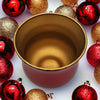 A metallic red glass tealight holder with a gold interior surrounded by festive glittery ornaments