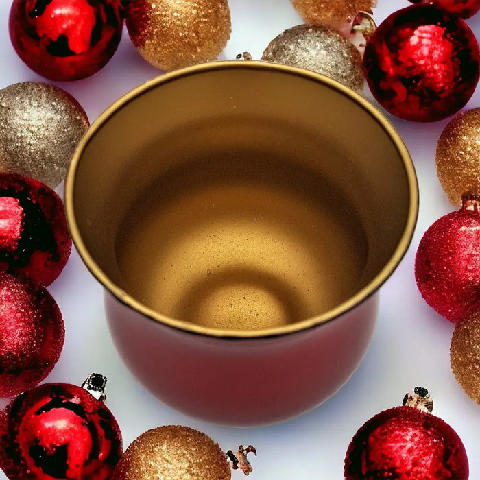 A metallic red glass tealight holder with a gold interior surrounded by festive glittery ornaments