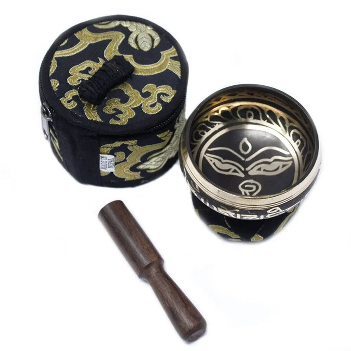 Black and gold mini singing bowl with intricate face design, wooden mallet, and embroidered carrying case