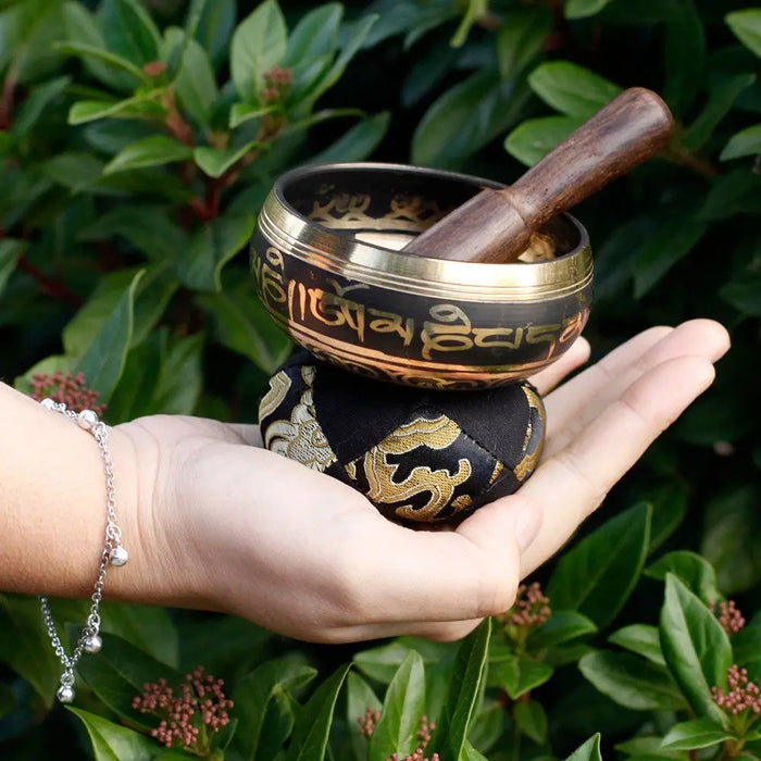 Black mini singing bowl with gold trim and engraved sanskrit script with wooden mallet resting inside