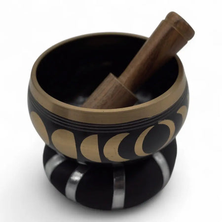 Black and gold Tibetan singing bowl set with moon phase design and wooden mallet used to release negative emotions