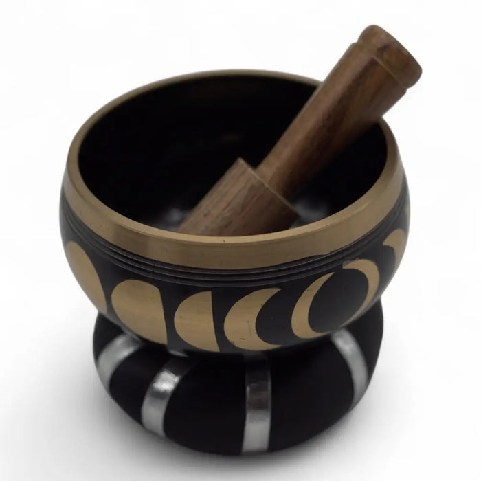Black and gold Tibetan singing bowl set with moon phase design and wooden mallet used to release negative emotions