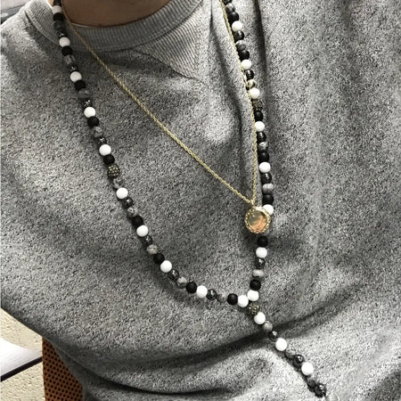Black white and gray beaded gemstone necklace with a gold toned angel wing pendant on a white background