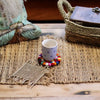 A small white ceramic teacup with blue pattern on a round multicolour felt ball coaster set of 4 coasters