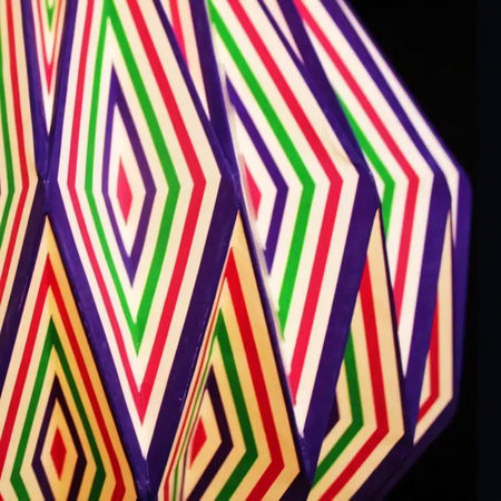 A multi-coloured origami light shade with bold red green and purple striped diamond patterns on cream paper