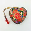 Hand-painted heart-shaped papier maché bauble with vibrant red green purple floral patterns and gold cord tassel