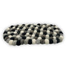 An oval-shaped multi-grey felt ball centre mat made of tightly woven fluffy wool balls in black white and grey shades