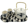 White ceramic teapot with black bamboo ink painting and red seal mark on multi-grey felt ball oval centre mat