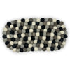 An oval centre mat made of interwoven black white and gray wool felt balls