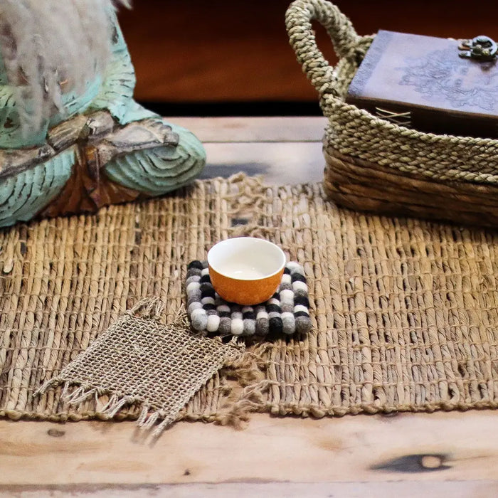 Orange ceramic tea cup on a square multi-grey felt ball coaster made of black white and gray felt balls