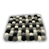 A square felt mat made of fluffy wool balls in black white and gray shades used as coasters in a set of 4