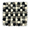 A square felt ball placemat made of woven wool balls in black white and shades of grey