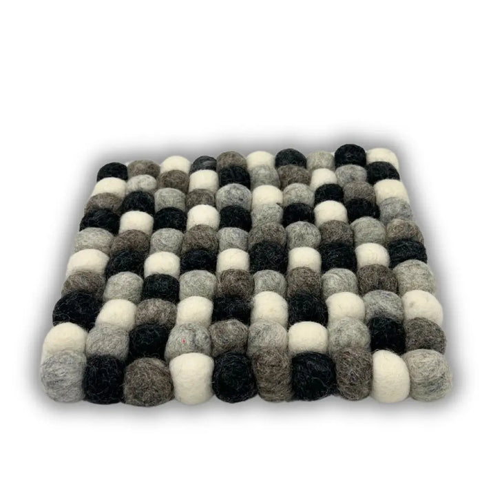 A square felt ball placemat made of fluffy wool balls in black white and various shades of grey