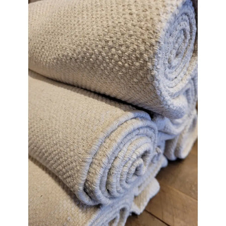 Natural 100% woven cotton mat shown as beige woven rug rolled and stacked neatly for home use