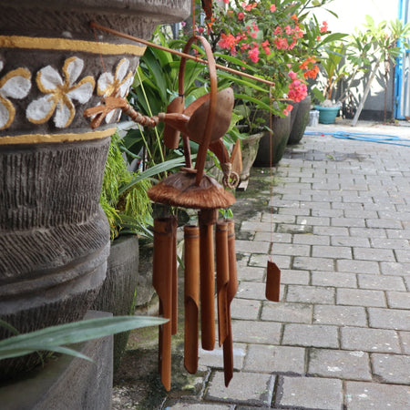 A rustic bronze bird top natural bamboo wind chime with bamboo tubes hanging below and coconut dragon accents