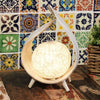A warm glowing coconut lamp with a textured surface in a whitewashed wooden frame with three slender legs