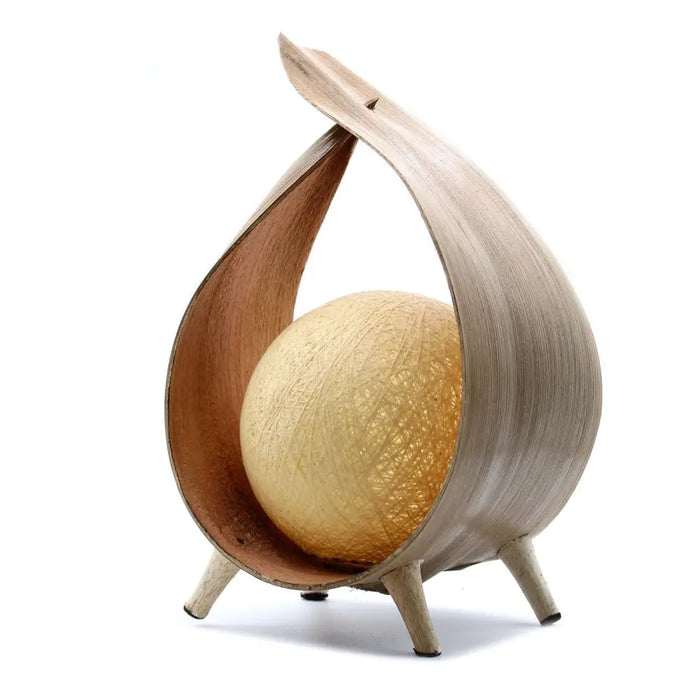 A natural coconut lamp with a warm golden spherical light inside a light wood curved frame with three slim legs