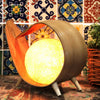 Natural coconut lamp with a warm glowing spherical light encased in a curved wooden frame with orange lining and three legs